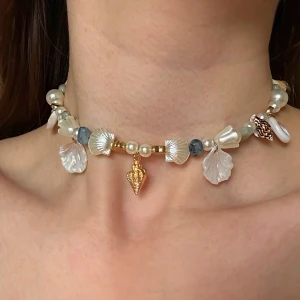 Pärlchoker och armband med snäckor - Unikt set med choker och armband dekorerade med vita och guldiga pärlor, blå stenar och snäckformade hängen. Både halsbandet och armbandet har detaljer i guld och skimrande snäckor som ger en strandig vibe. Perfekt för dig som vill sticka ut med coola accessoarer.