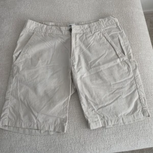 Beige bomullsshorts med fickor - Snygga beige shorts i bomull med klassisk passform och två sidofickor. Perfekta för varma dagar och enkla att matcha med det mesta. Stängs med knapp och dragkedja framtill. Stilrena och bekväma för en avslappnad look.