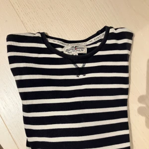 Randig långärmad tröja Hampton Republic - Snygg långärmad tröja från Hampton Republic i marinblått och vitt med klassiskt randigt mönster. Tröjan har broderad logga på ärmen och är tillverkad i mjuk bomull.