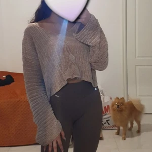 Beige ribbad croppad kofta - Säljer en beige ribbad kofta med croppad passform och långa, vida ärmar. Koftan har v-ringning och knappar framtill, vilket ger en chill och trendig look. Perfekt att slänga på sig över ett linne eller t-shirt.