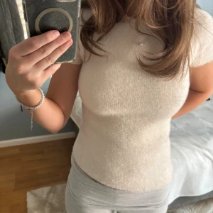 Ljusbeige topp med fuskpäls och knytningar i ryggen - Superfin ljusbeige topp med korta ärmar och går ner snett längst ner på toppen(kan se på bild 4) Toppen har en snygg öppen rygg med knytband som ger en unik look. Sååå skön och fluffig tröja. Använd endast en gång💗💗