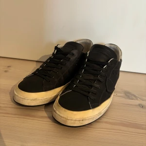 Philippe Model svarta sneakers i skinn - PRIS KAN DISKUTERAS Svarta sneakers från Philippe Model i skinn med vita kontrastsömmar och beige sula. Skorna har svarta skosnören, rund tå och silverdetalj på hälen. Klassisk låg modell med logga på sidan och bekväm platt sula.