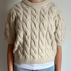 Beige stickad tröja från Gina Tricot - Superfin beige stickad tröja från Gina Tricot med korta puffärmar och flätmönster. Tröjan har rund halsringning och ribbade muddar. Perfekt för lager-på-lager och ger en mysig vibe till din outfit. Andvänd 2 gånger!