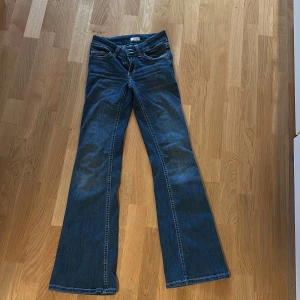 Blå bootcut jeans från Nelly - Snygga blå jeans från Nelly med bootcut-modell och klassisk femficksdesign. Jeansen har en mörk tvätt och coola detaljer på bakfickorna med kontrastsömmar. 