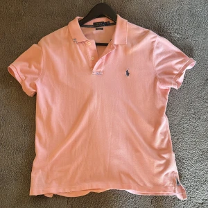 Ljusrosa pikétröja från Polo Ralph Lauren - Snygg ljusrosa pikétröja från Polo Ralph Lauren med klassisk krage, knappar och broderad logga på bröstet. Tillverkad i mjuk bomull och har korta ärmar. Perfekt för en chill och stilren look. Priset är inte hugget i sten.