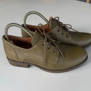 Olivgröna skinnskor från Cinnamon - Snygga olivgröna skor från Cinnamon i äkta skinn. Skorna har klassisk snörning, låg klack och rund tå. Perfekta för dig som gillar stilrena och bekväma skor med en tidlös look.