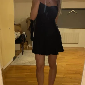 Svart blommig kort klänning - Supersnygg svart kort klänning med tunna axelband och subtilt blommönster i tyget. Klänningen har en lätt utsvängd kjol och figurnära passform upptill. Perfekt för dig som vill ha en stilren men ändå unik look.