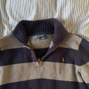 Polo Ralph Lauren tröja stickad - Randig stickad tröja från Polo Ralph Lauren i marinblått och grått. Tröjan har halv dragkedja, hög ribbad krage och broderad logga på bröstet. Perfekt för dig som gillar klassisk och sportig stil. Köpt för 1100kr
