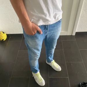 Dondup George jeans - Säljer ett par ljusblå skinny jeans från dondup i storlek 34. Jeansen har klassisk femficksdesign, snygga slitningar och smal passform. Tillverkade i mjukt denimtyg med orangea sömmar och diskret logga bak i midjan. Perfekta för en avslappnad och trendig look.
