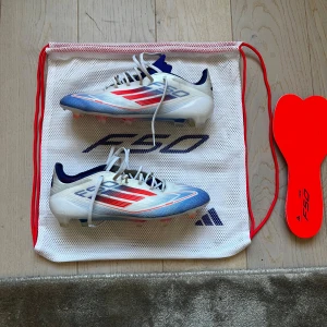 Adidas F50 fotbollsskor blå/röd/vit - Säljer ett par Adidas F50 fotbollsskor i vitt med blå och röda detaljer. Skorna har inte använts så mycket men har några små defekter. Kommer med extra sulor och bag till. Pris kan diskuteras.