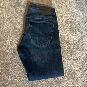 Jack & Jones Glenn - Snygga blå jeans från Jack & Jones, modell Slim Glenn. Jeansen har en slim passform, klassisk femficksdesign och snygga slitningar. Tillverkade i stretchig denim för extra komfort. Perfekta för dig som gillar en smal siluett och stilren look.