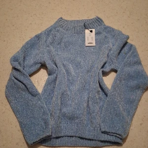 Blå stickad tröja från 157 - Mysig ljusblå stickad tröja från 157 💘med ribbad krage, ärmslut och nederkant. Perfekt för kyliga dagar och enkel att matcha med jeans eller kjol. Tröjan har en klassisk passform och är långärmad för extra komfort