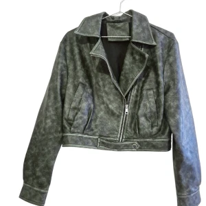 Grön biker skinnjacka  - Snygg grön/mörkgrön/army green skinnjacka i bikerstil med sned dragkedja och krage. Jackan har två fickor framtill och en kort, croppad passform. Materialet är syntetiskt skinn med en matt finish och coolt tvättad look. Jackan är helt ny & oanvänd 