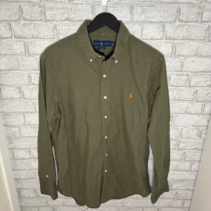 Ralph Lauren skjorta - Unik olivgrön ralph Lauren skjorta med orange logga som ger en snygg kontrast. Bra skick och lätt att matcha både till vardag och mer uppklätt. Hör av dig vid intresse 🙌