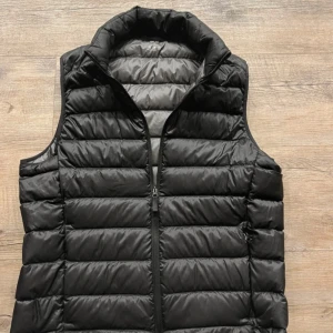 Svart Uniqlo väst - Stilren svart ultra light väst från Uniqlo. Västen har en hel dragkedja framtill och två sidofickor med dragkedja. Perfekt att slänga över en hoodie eller tröja för extra värme. Enkel och clean design som funkar till många outfits.