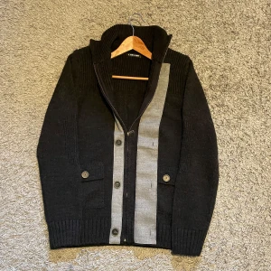 Svart kofta med grå detaljer Y Two Knit - Säljer en trendig stilren svart cardigan, med zip! 🙌🏻Perfekt för kalla dagar! ❄️Tröjan är i nyskick 9,5/10. Tröjan har en klassisk zip och knappar upp till med en stil som siktar på ”oldmoney”. Tveka inte på att höra av er!💪🏼