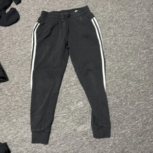 Svarta Adidas mjukisbyxor med vita ränder - Svarta mjukisbyxor från Adidas med klassiska vita ränder längs bena ni står för frakten!