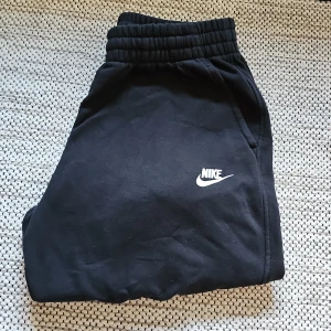 Svarta mjukisbyxor från Nike XL - Svarta mjukisbyxor från Nike i storlek XL, med klassisk vit Nike-logga broderad på benet. Byxorna har resår i midjan och är tillverkade i mjuk bomullsmix som känns skön mot huden. Perfekta för chill eller träning. Säljer för att dem har blivit för små för mig. Min kamra är lite sisådär dålig därför är bilderna inte av så hög kvalitet. Om ni vill ha bättre bilder säg bara till. Priset är inte suttit i sten.