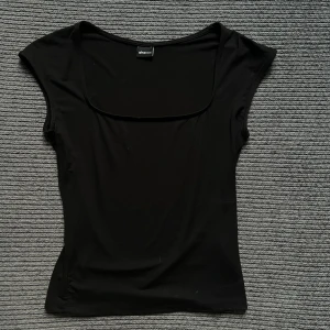 Svart topp Gina Tricot - Svart topp från Gina Tricot med snygg fyrkantig ringning och korta ärmar. Tight i passform. Skriv om ni har nå funderingar <3