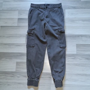 Grå cargopants från ONLY, strl 36/32 - Snygga grå cargopants från ONLY med resår vid bensluten och stora fickor på sidorna. Byxorna har normal passform och är tillverkade i mjuk bomull. Perfekta för en avslappnad och trendig look.