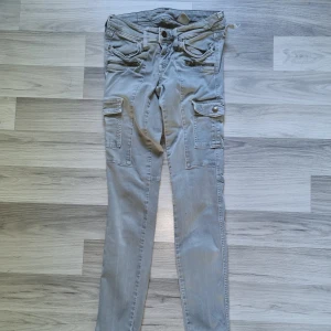 Gröngråa cargopants med dragkedjor - Snygga gröngråa cargopants med flera fickor på benen och coola dragkedjedetaljer framtill. Byxorna har raka ben och är tillverkade i bomullsmaterial. Perfekta för en avslappnad streetstil. Se defekterna på bild. 