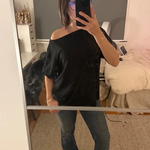 Svart offshoulder topp i bomull - Säljer en svart offshoulder topp med lös passform och trekvartsärm. Toppen är i mjuk bomull och har en avslappnad vibe med ena axeln bar. Perfekt att styla med jeans eller kjol för en chill look.