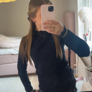 Svart ribbad tröja från Name It - Svart långärmad tröja från Name It i ribbad bomull. Tröjan har en tight passform och rund halsringning. Perfekt basplagg med stilren look och stretchigt material som sitter snyggt på kroppen.