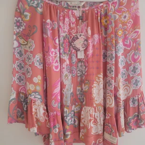 Blommig blus från Odd Molly 36 - Supersöt blommig blus från Odd Molly i färgen soft red med inslag av rosa, vitt, gult och grått. Långärmad modell med volangdetaljer vid ärmslut och nederkant, samt rynk och veck framtill. Luftig och flowy passform, perfekt för vår och sommar.