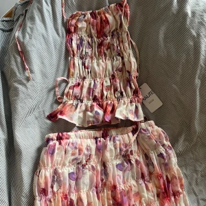 Blommig volangig set - Supersöt linnetopp, med med knyt i sidorna. Matchande långkjol till. Jättefint, passar till lite finare tillställningar. 