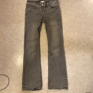 Grå bootcut jeans från Gina Tricot - Grå jeans från Gina Tricot i bootcut-modell med snygga detaljer på bakfickorna, som broderade mönster och silvriga knappar. Jeansen har klassisk femficksdesign och är tillverkade i mjukt bomullstyg med en skön passform.