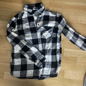 Rutig skjorta från H&M Divided XS - Snygg rutig skjorta från H&M Divided i svart och vitt. Skjortan har klassisk krage, bröstficka och knäppning framtill. Perfekt för en avslappnad och cool stil. Tillverkad i mjuk bomull och har långa ärmar.