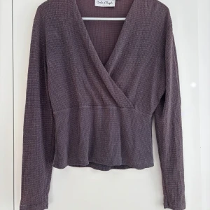 Lila omlottopp från Carla d'Angelo - En lila omlottopp från Carla d'Angelo med lång ärm och v-ringning. Tröjan är glittrig och passar som en fest topp eller när man vill bara ha lite extra bling✨skriv om du har frågor💗