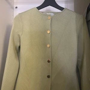 Ljusgrön kofta från Zara med guldknappar - Supersnygg ljusgrön kofta från Zara i stickad bomullsmix. Rak modell med rund halsringning och stilrena guldknappar framtill. Perfekt att slänga över en topp för en clean look. Långärmad och enkel att matcha med det mesta.