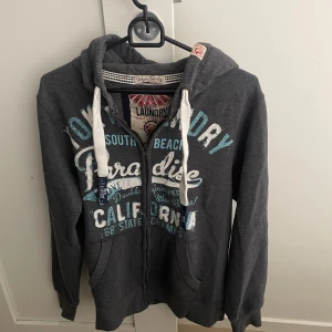 Mörkgrå zip hoodie från Tokyo Laundry - Mörkgrå zip hoodie från Tokyo Laundry i storlek S, modellen är ca 180cm lång. Hör av dig vid funderingar!