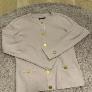 Rosa kofta från STOCKH LM med guldknappar - Snygg rosa kofta från STOCKH LM med rund halsringning och guldiga knappar framtill och på ärmslut. Koftan har två små fickor framtill och är perfekt till hösten! Säljer en i svart och mörkblå också! 