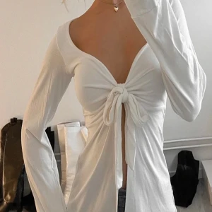 Vit långärmad omlottopp med knyt - Supersnygg vit långärmad topp med djup v-ringning och knyt framtill. Ifrån design by si, Modellen är omlott och har en croppad känsla med lätt utsvängda ärmar. Perfekt för dig som gillar en feminin och trendig stil. Tunn och mjuk i materialet, passar till både jeans och kjol. Xs/s