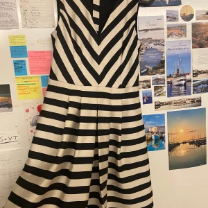 Randig klänning - Snygg kortklänning från Banana Republic i svart och beige med breda ränder och v-ringning. Klänningen är ärmlös, har markerad midja och dragkedja bak. Materialet känns stadigt och har en lätt glans. Perfekt för dig som gillar grafiska mönster och stilren design.