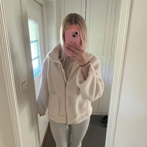 Beige teddyjacka med dragkedja - Mysig beige teddyjacka med hög krage och dragkedja framtill. Perfekt för kalla dagar när du vill vara både varm och snygg. Materialet är fluffigt och mjukt fleece🩷