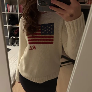 Vit stickad tröja Polo Ralph Lauren - Snygg vit stickad tröja från Polo Ralph Lauren med amerikansk flagga och RL-broderi på bröstet. Storlek L men skulle säga M. Tröjan är i 100% bomull, har rund hals och långa ärmar med breda ribbade muddar. Perfekt för dig som gillar klassisk och chill stil.
