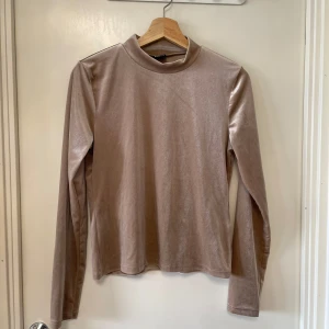 Beige sammets polotröja Gina Tricot - Säljer en beige polotröja i mjuk sammet från Gina Tricot. Tröjan har lång ärm och en enkel, stilren design med lätt glansigt tyg. Perfekt för dig som gillar en clean och trendig look.