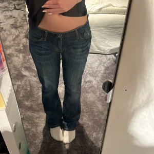 Levi's Skinny Boot jeans blå - Säljer ett par Levi's Skinny Boot jeans i mörkblå tvätt med snygga slitningar. Modellen har låg midja och bootcut-ben, klassiska femficksdetaljer och Levi's signatur på bakfickorna. Perfekta om du gillar en smal passform upptill och lite utsvängda ben. Säljer då de är lite för stora i midjan