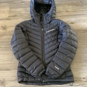 Svart dunjacka Peak Performance XS - Svart dunjacka från Peak Performance i storlek women XS. Jackan har huva, dragkedja framtill och quiltad design. Tillverkad i polyester och dun, perfekt för kalla dagar. Snygg och sportig look med logga på bröstet och ärmen. Ett litet hål har blivit lagat med en lapp på armen annars mycket fint skick. Nypris ca 3000, mitt pris 400 men såklart diskuterbart, bara att höra av sig vid frågor