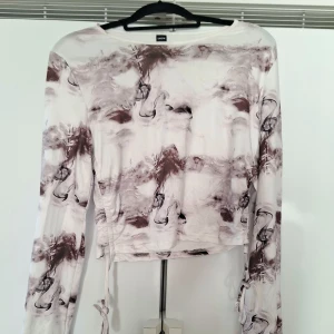Vit och brun croppad långärmad topp - Säljer en croppad långärmad topp från Shein med abstrakt mönster i vitt och brunt. Toppen har snörning i sidorna och är tillverkad i ett mjukt, stretchigt material. Perfekt för dig som gillar unika prints och trendiga detaljer.Är XL men känns mer som. M/L