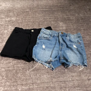 2-pack shorts, svarta & blå jeans, stl 152 - Säljer två par shorts i storlek 152. Ena paret är svarta, klassiska och stilrena med fickor. Det andra paret är ljusblå jeansshorts med slitna detaljer och fransig kant nertill för en cool look. Båda har knapp och dragkedja framtill.