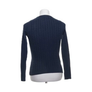 Mörkblå kabelstickad tröja Lexington XS - Kabelstickad mörkblå tröja från Lexington i klassisk modell med rund halsringning och diskret logga på bröstet. Tröjan har lång ärm och ribbade muddar, perfekt för dig som gillar en stilren och tidlös look.