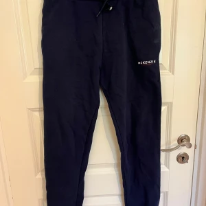 Mörkblå mjukisbyxor från McKenzie - Mörkblå mjukisbyxor från McKenzie med dragsko i midjan och logga på ena benet. Byxorna har en klassisk, avslappnad passform och är tillverkade i mjukt bomullsmaterial. Perfekta för chill dagar eller när du vill vara bekväm. Storlek XL för barn. 