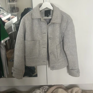 Grå kappa - Säljer en stilren grå kappan från Lager 157 Jackan har raka linjer, stora fickor framtill, klassisk krage och knäppning med knappar. Perfekt för dig som gillar minimalistisk och clean stil.