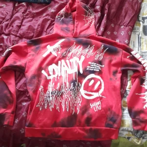 Röd hoodie från New Yorker - Säljer en röd och svart hoodie från Black Squad med stora vita tryck, graffitistil och coola detaljer som dödskalle, taggar och spindelnät. Hoodien har huva och relaxed fit, perfekt för dig som gillar streetwear och unika plagg.