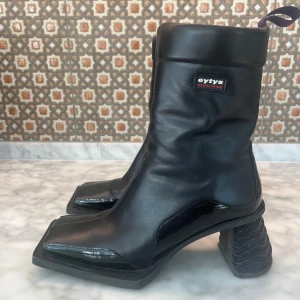 Svarta boots med klack från Eytys - Unika svarta boots från Eytys i skinn med fyrkantig tå och chunky, vågformad klack. Dragkedja på insidan och diskret logga på skaftet. Snygg, futuristisk design som sticker ut och passar perfekt till streetwear eller edgy outfits.