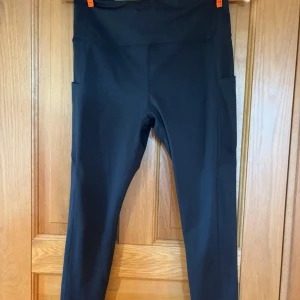 Svarta höga leggings med fickor - Svarta leggings med hög midja och praktiska sidofickor. Tight passform och stretchigt material som passar perfekt till träning eller chill. Snygg och enkel design som är lätt att matcha med andra plagg.